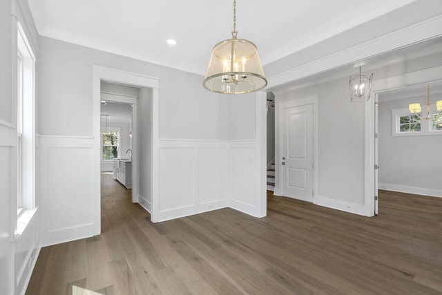 unfurnished dining area with a chandelier, ornamental molding, a wainscoted wall, and wood finished floors