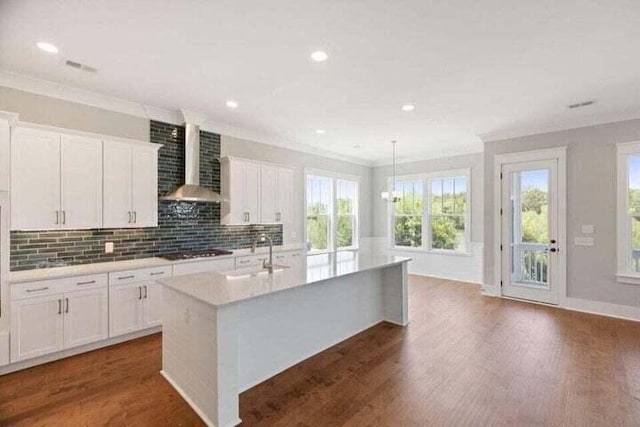 kitchen with dark wood finished floors, stovetop, a sink, and wall chimney range hood