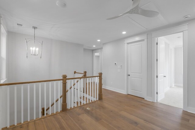 corridor with recessed lighting, wood finished floors, visible vents, baseboards, and an upstairs landing