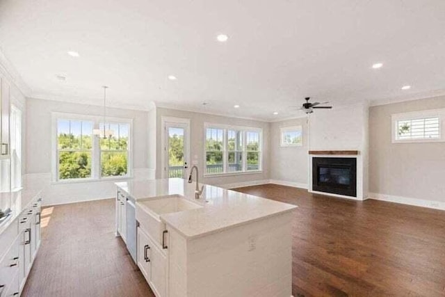 kitchen featuring a kitchen island with sink, white cabinets, ornamental molding, dark wood-style floors, and a glass covered fireplace