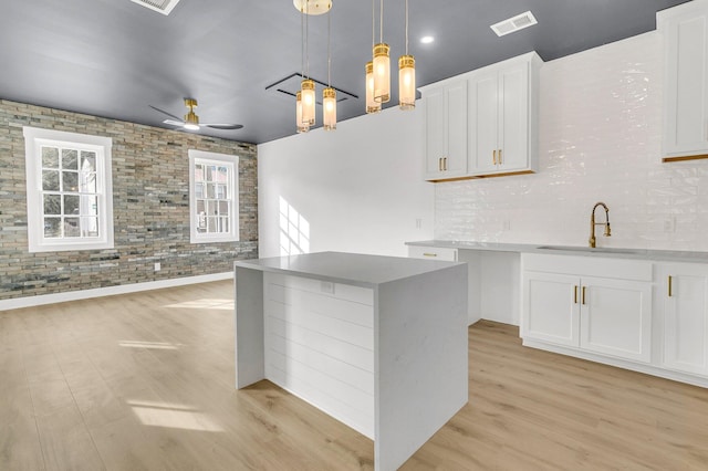 kitchen featuring white cabinetry, sink, brick wall, pendant lighting, and light wood-type flooring