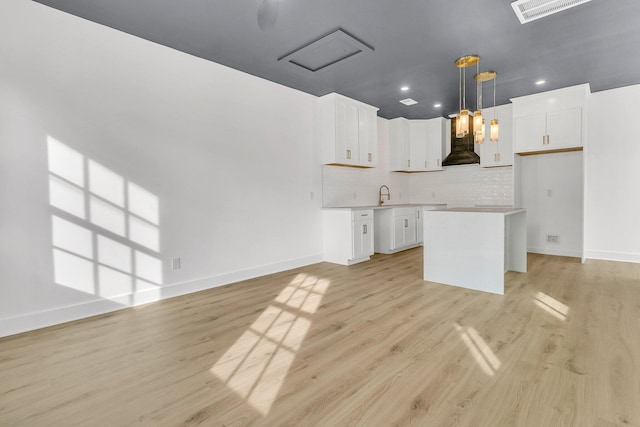 kitchen with decorative backsplash, wall chimney range hood, pendant lighting, a center island, and white cabinetry