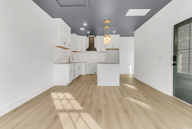 kitchen with wall chimney exhaust hood, sink, light hardwood / wood-style flooring, white cabinetry, and hanging light fixtures