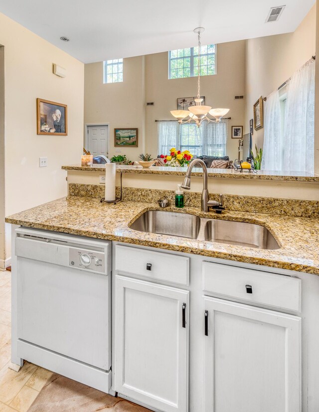 kitchen with white dishwasher, light stone counters, sink, and white cabinetry