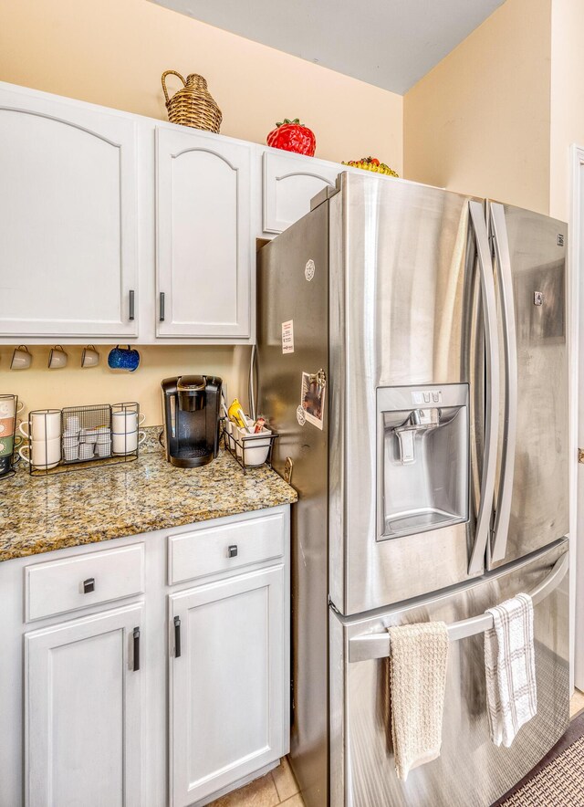 kitchen featuring stainless steel refrigerator with ice dispenser, light tile patterned flooring, light stone counters, and white cabinets