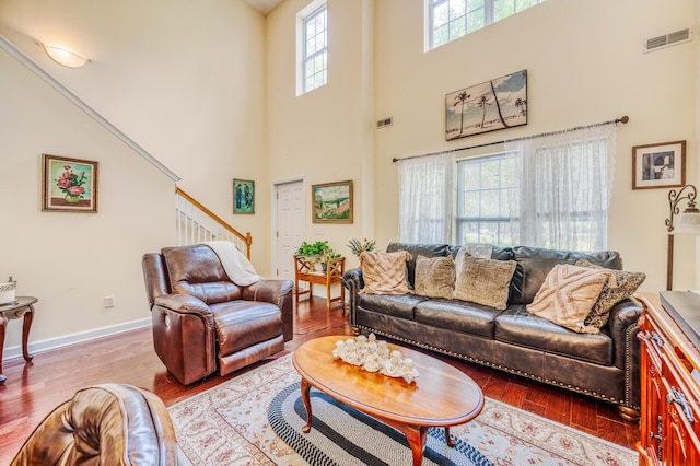 living area with visible vents, wood finished floors, a high ceiling, baseboards, and stairs