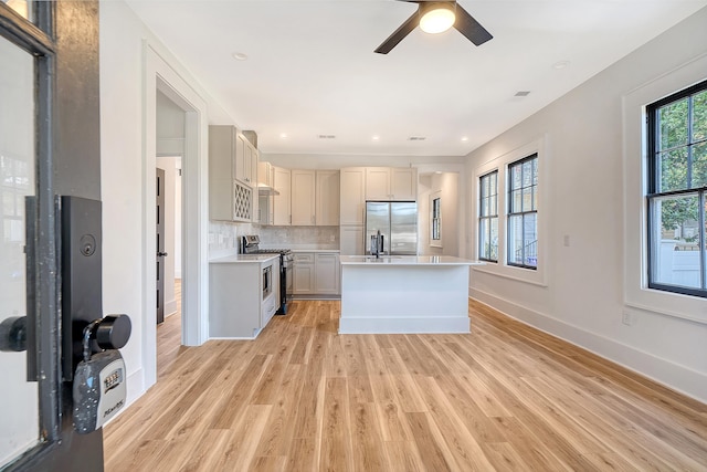 kitchen featuring backsplash, ceiling fan, light wood-type flooring, a kitchen island, and stainless steel appliances