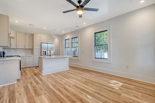 kitchen featuring ceiling fan, backsplash, stainless steel fridge, light hardwood / wood-style floors, and a center island with sink