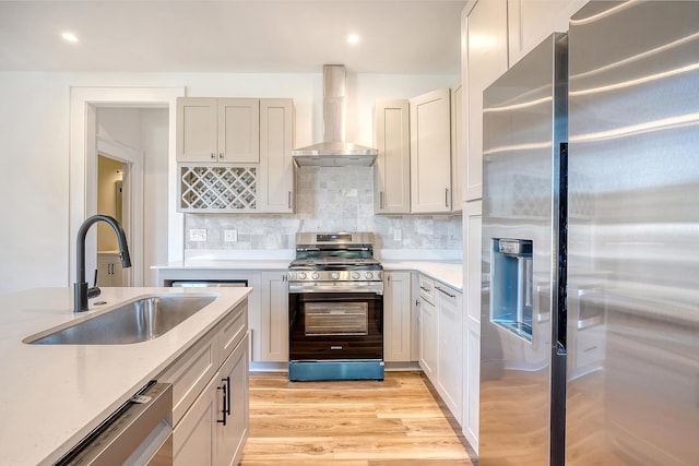 kitchen with sink, stainless steel appliances, wall chimney range hood, backsplash, and light wood-type flooring