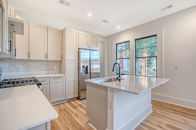 kitchen with sink, gas range oven, stainless steel refrigerator with ice dispenser, light hardwood / wood-style floors, and a center island with sink