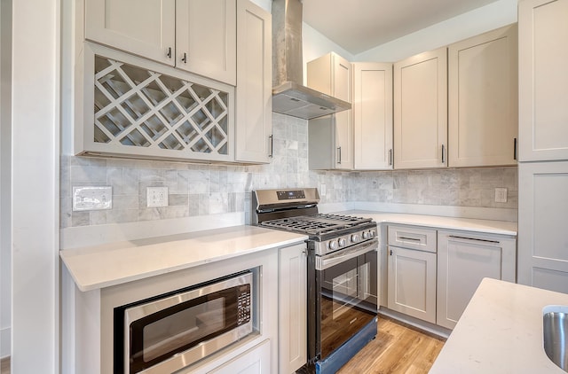 kitchen featuring decorative backsplash, wall chimney range hood, stainless steel appliances, and light hardwood / wood-style flooring