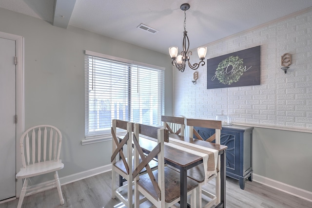 dining space with a notable chandelier, beam ceiling, a textured ceiling, and light hardwood / wood-style flooring