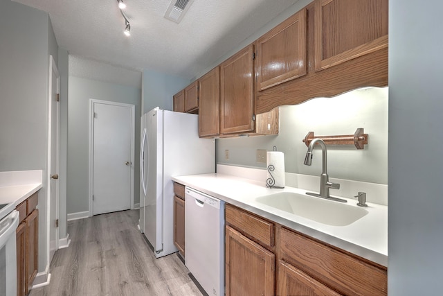 kitchen featuring stove, white dishwasher, sink, light hardwood / wood-style flooring, and a textured ceiling