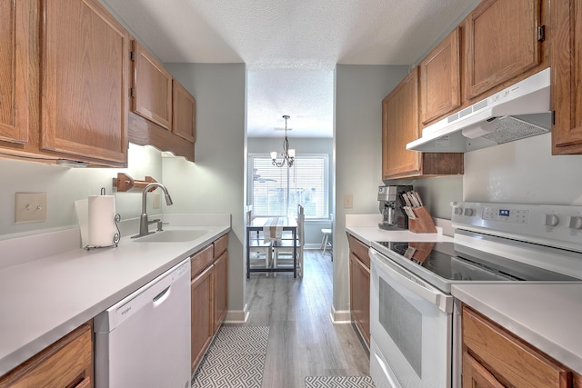 kitchen with pendant lighting, white appliances, sink, a notable chandelier, and light hardwood / wood-style floors