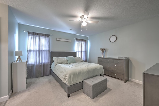 bedroom with ceiling fan, light colored carpet, and a textured ceiling