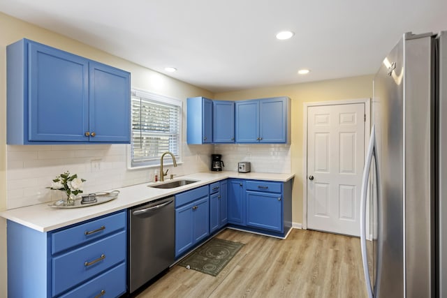 kitchen featuring blue cabinets, sink, light wood-type flooring, stainless steel appliances, and backsplash