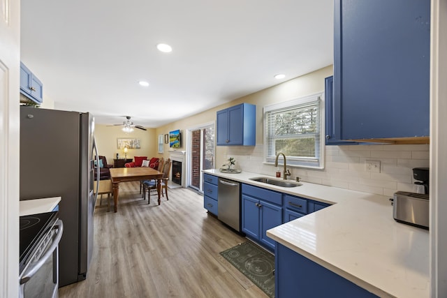 kitchen with sink, decorative backsplash, stainless steel appliances, blue cabinetry, and light hardwood / wood-style flooring