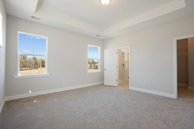 unfurnished bedroom with a walk in closet, a tray ceiling, light colored carpet, and visible vents