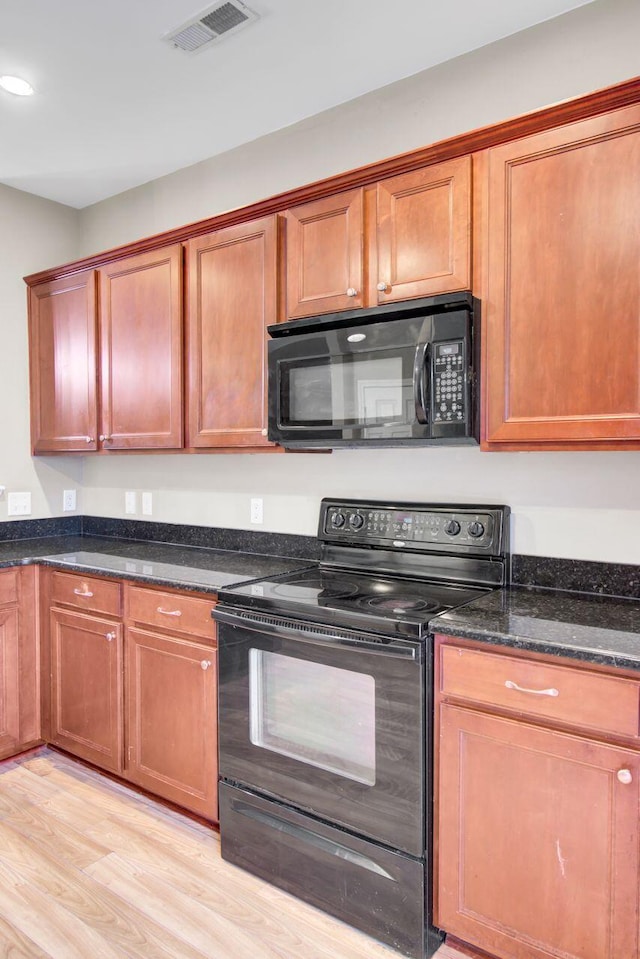 kitchen with light hardwood / wood-style floors, dark stone counters, and black appliances