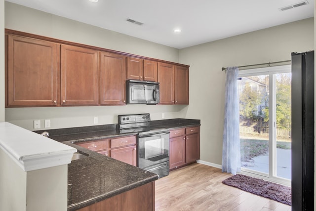 kitchen with dark stone counters, light hardwood / wood-style floors, sink, stainless steel refrigerator, and electric range