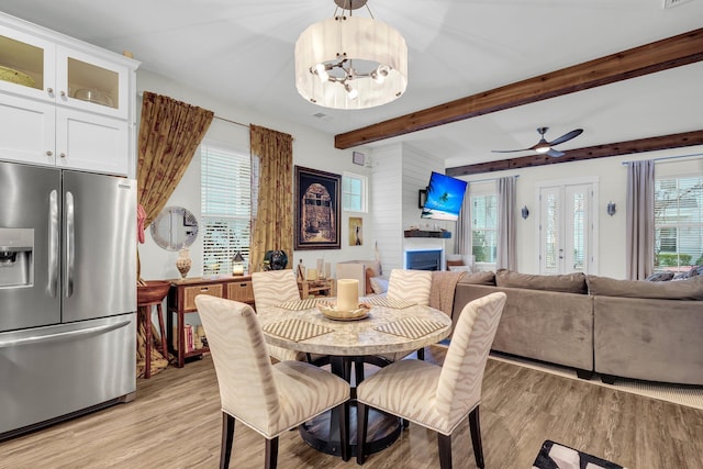 dining area with beam ceiling, a wealth of natural light, ceiling fan with notable chandelier, and light wood-type flooring