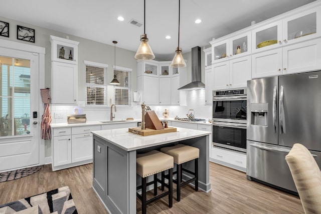 kitchen featuring stainless steel appliances, white cabinets, a kitchen island, decorative light fixtures, and wall chimney exhaust hood