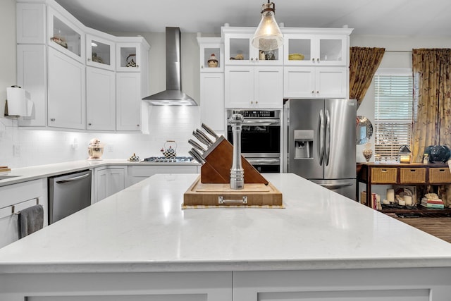 kitchen featuring tasteful backsplash, white cabinetry, hanging light fixtures, stainless steel appliances, and wall chimney exhaust hood