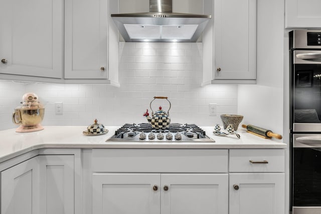 kitchen featuring wall chimney range hood, stainless steel appliances, and white cabinets