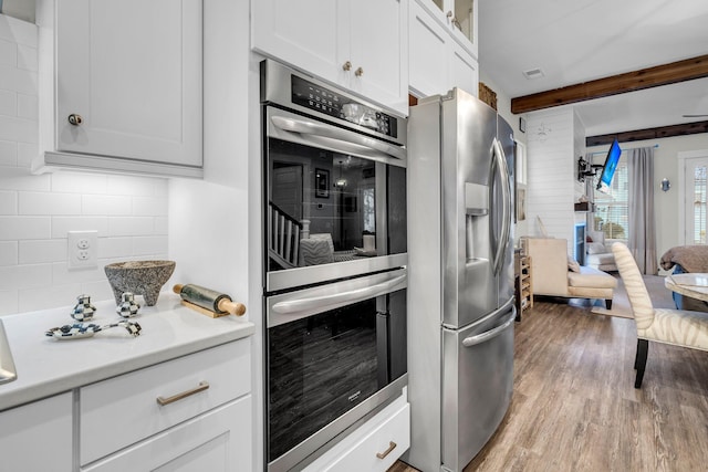 kitchen featuring white cabinetry, tasteful backsplash, light wood-type flooring, stainless steel appliances, and beam ceiling