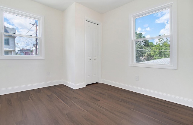 unfurnished bedroom with dark wood-type flooring, multiple windows, and a closet