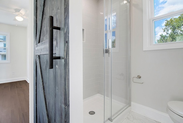 bathroom featuring hardwood / wood-style floors, ceiling fan, toilet, and a shower with door