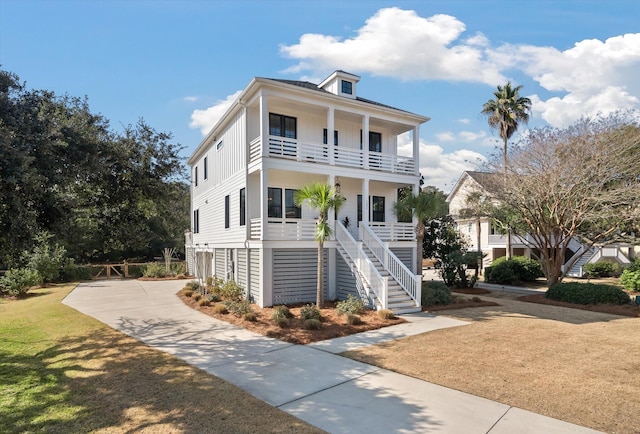 raised beach house with driveway, a balcony, stairway, a porch, and a front yard