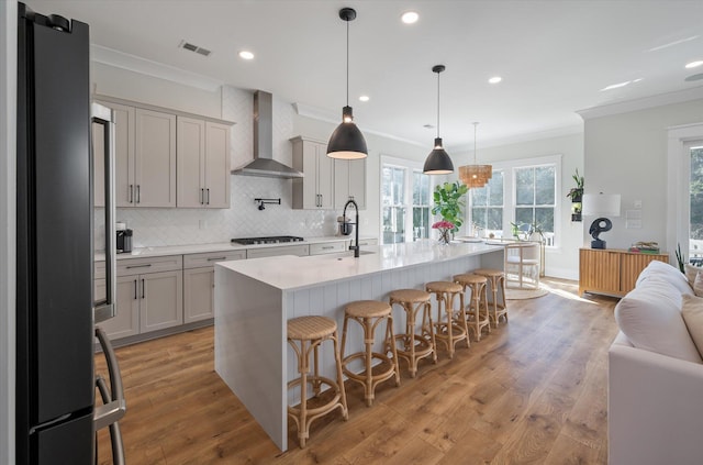 kitchen featuring light wood-style floors, wall chimney exhaust hood, ornamental molding, light countertops, and black appliances