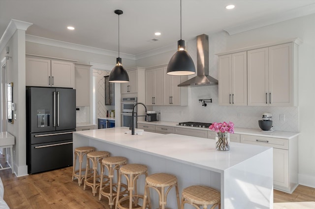 kitchen with wall chimney exhaust hood, light wood-style flooring, double oven, gas stovetop, and high end black refrigerator