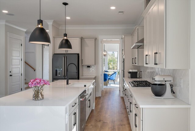 kitchen with under cabinet range hood, stainless steel appliances, visible vents, an island with sink, and crown molding