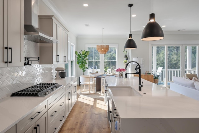 kitchen featuring stainless steel gas cooktop, wall chimney range hood, ornamental molding, light wood-type flooring, and decorative backsplash