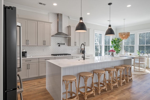 kitchen with light wood finished floors, visible vents, freestanding refrigerator, black stovetop, and wall chimney range hood