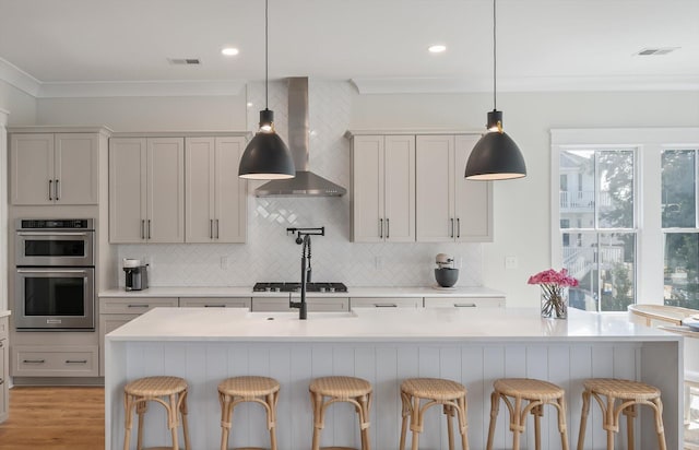 kitchen with double oven, visible vents, light countertops, wall chimney range hood, and crown molding