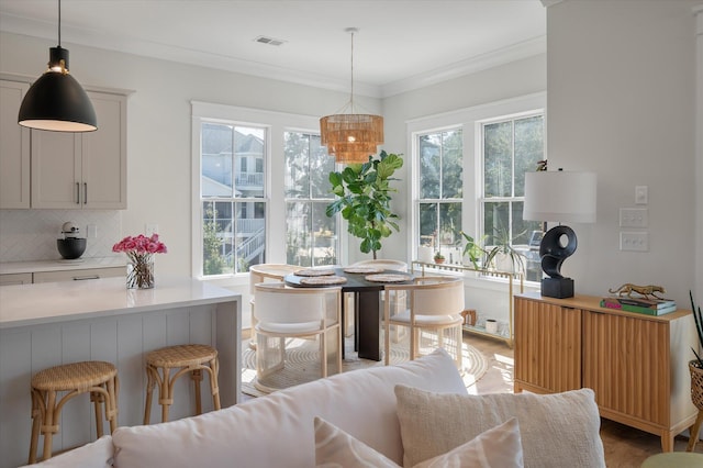 dining room with light wood finished floors, crown molding, visible vents, and a wealth of natural light