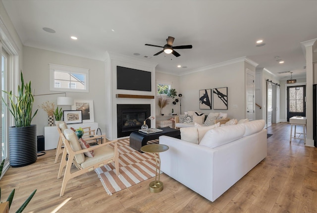 living room featuring ornamental molding, a large fireplace, a barn door, and light wood-style floors