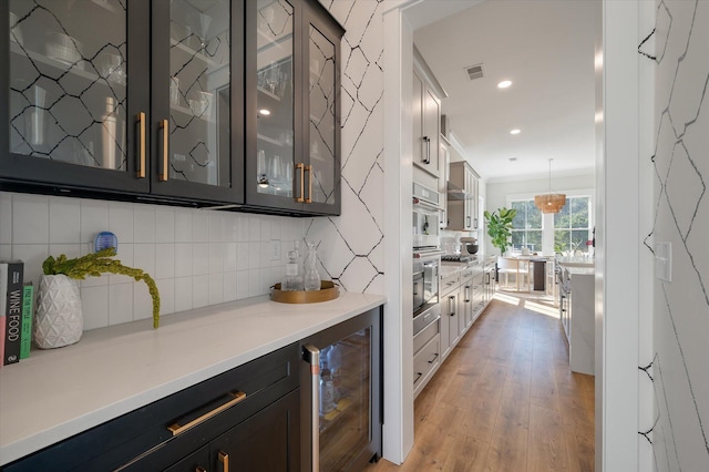 bar featuring beverage cooler, visible vents, decorative backsplash, light wood finished floors, and decorative light fixtures