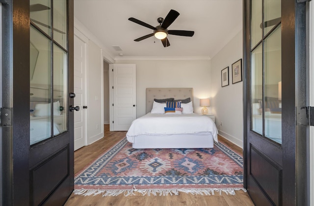 bedroom with ceiling fan, wood finished floors, visible vents, baseboards, and crown molding