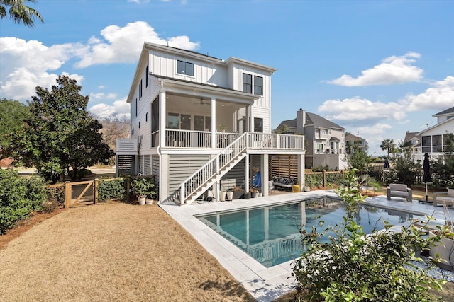 rear view of property with an outdoor pool, a sunroom, stairway, fence, and board and batten siding