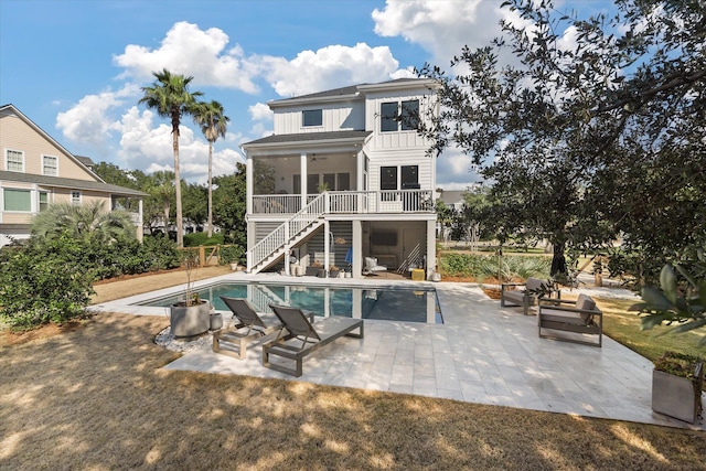 rear view of house featuring a patio, board and batten siding, a ceiling fan, an outdoor pool, and stairs