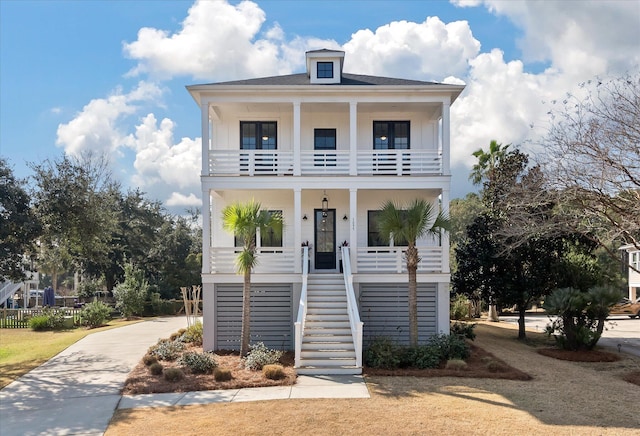 beach home with a porch, a balcony, driveway, stairway, and board and batten siding