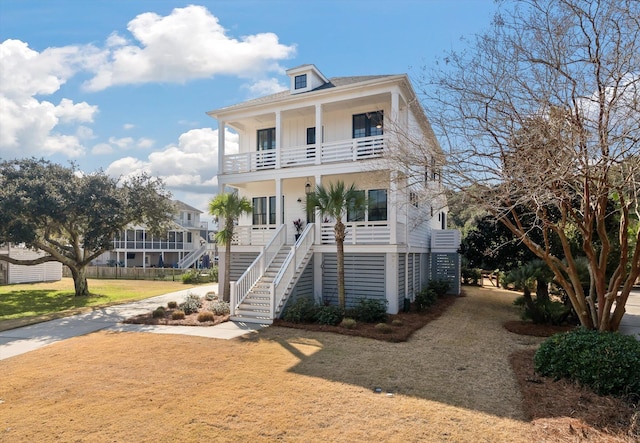 raised beach house with a porch, a balcony, stairs, driveway, and board and batten siding