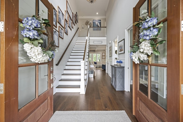 foyer entrance featuring dark wood-style floors, stairway, ornamental molding, and a towering ceiling