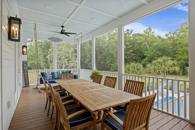 sunroom featuring a ceiling fan, outdoor lounge area, view of wooded area, and outdoor dining space