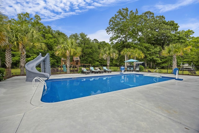 view of pool featuring a water slide, fence, view of scattered trees, and a patio area