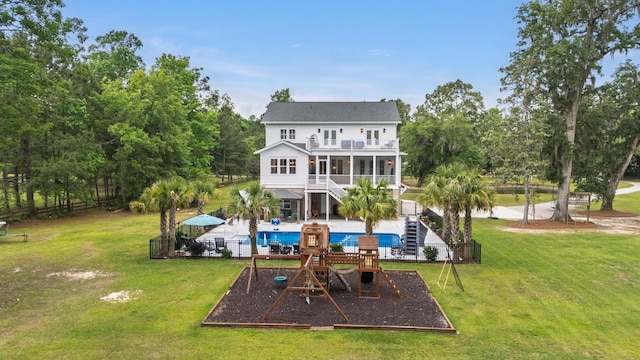rear view of property with a balcony, a sunroom, stairway, a patio, and a playground